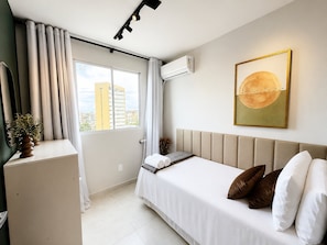 Una habitación de hotel moderna con cama, escritorio, ventana con cortinas, aire acondicionado y vista a la ciudad.