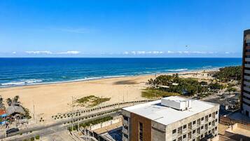 A coastal cityscape with a beach, a road with cars, and a building with a flat roof.