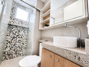 Un bagno moderno con doccia in vetro, lavandino bianco e mobiletto in legno.