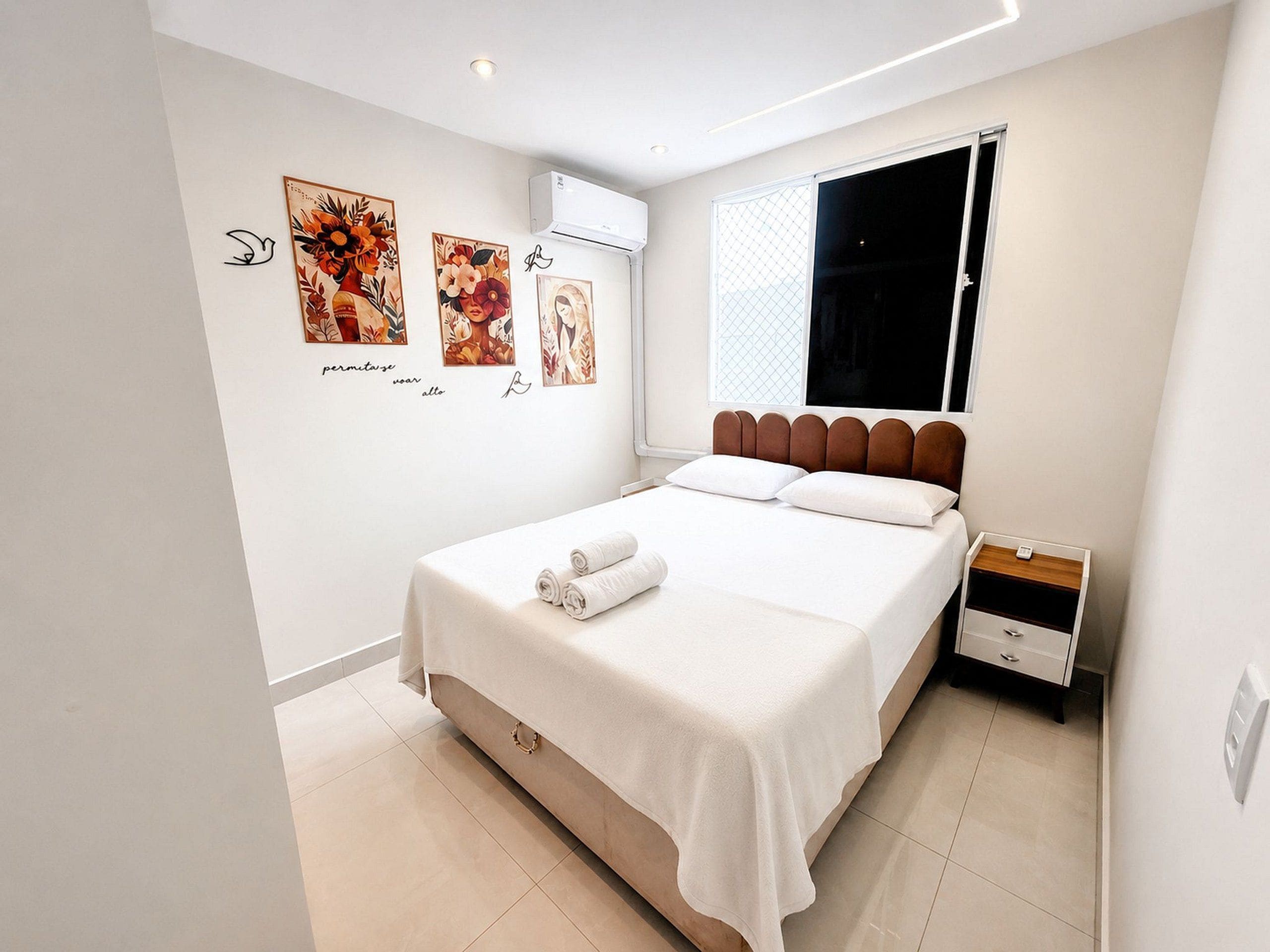 Une chambre à coucher avec un lit, une table de chevet, une fenêtre et des œuvres d’art murales.