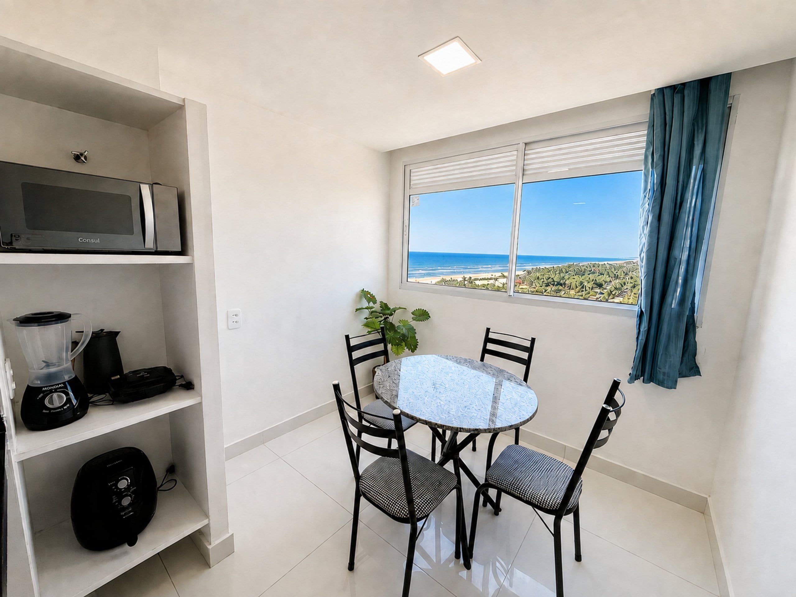 Un pequeño comedor con una mesa y sillas, un microondas sobre la mesa y una ventana con vista a la playa.