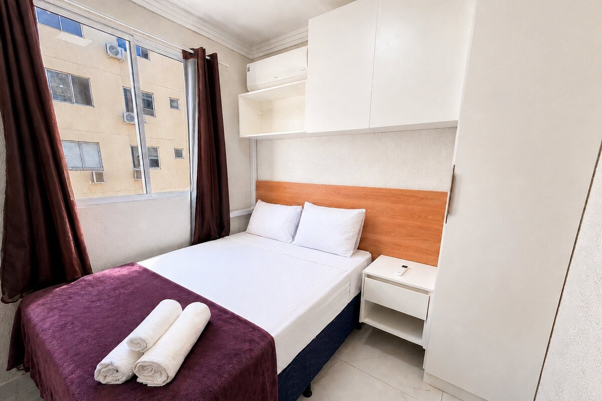 Una camera d'albergo con un letto, un comodino, un armadio e una finestra con tende.