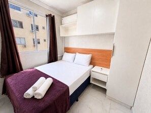 A hotel room with a bed, a nightstand, a wardrobe, and a window with curtains.