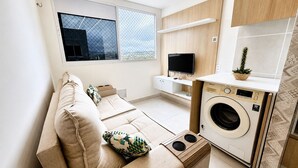 Een knus woongedeelte met een bank, een wasmachine, een televisie en een raam met uitzicht.