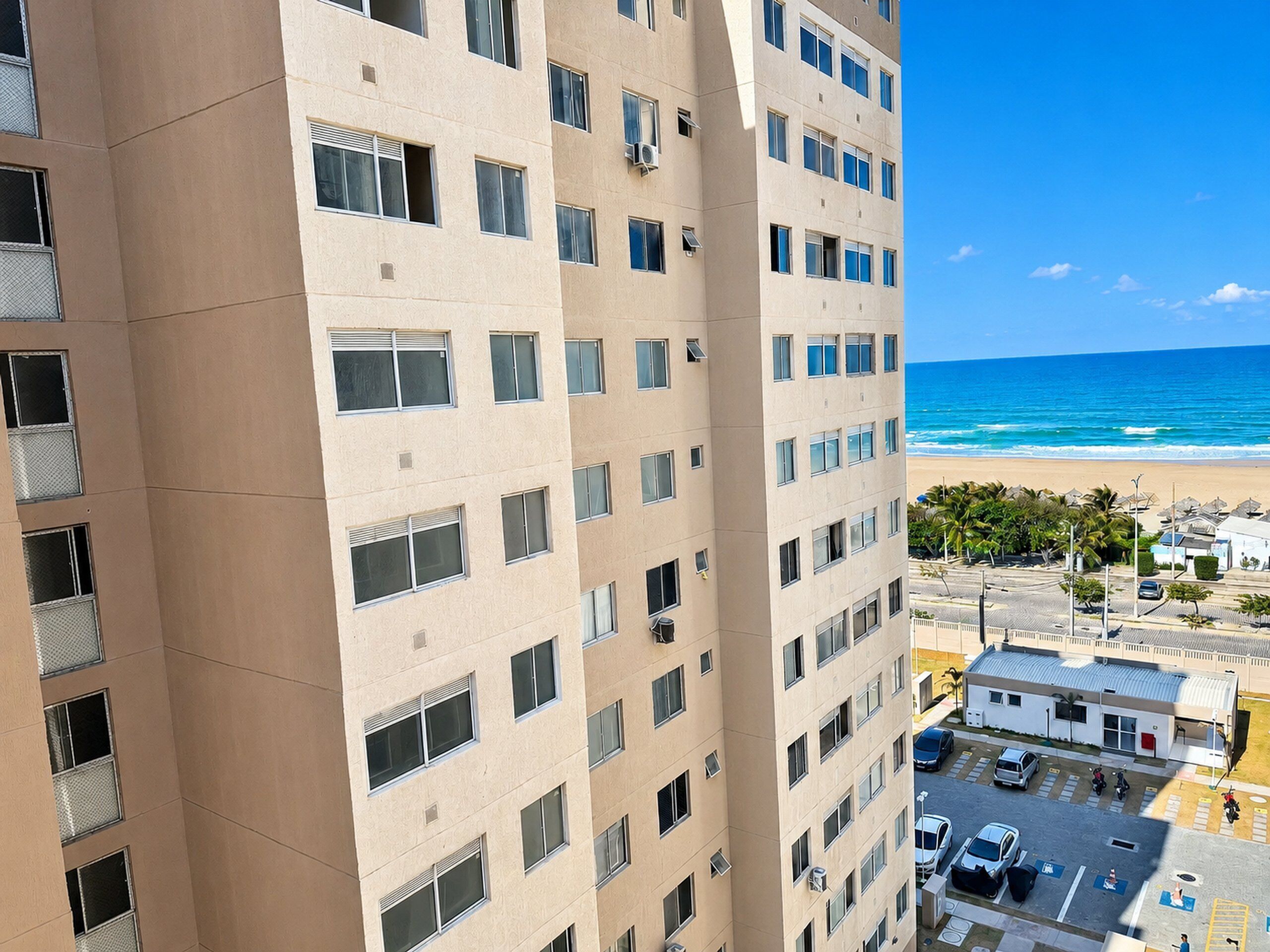 Um edifício alto com várias janelas, área de estacionamento e vista para a praia.