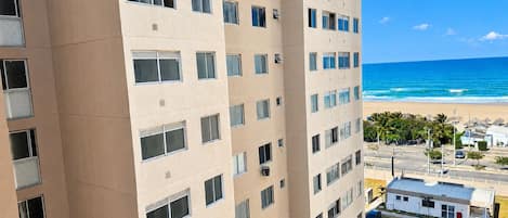 A high-rise building with multiple windows, a parking area, and a beach view.