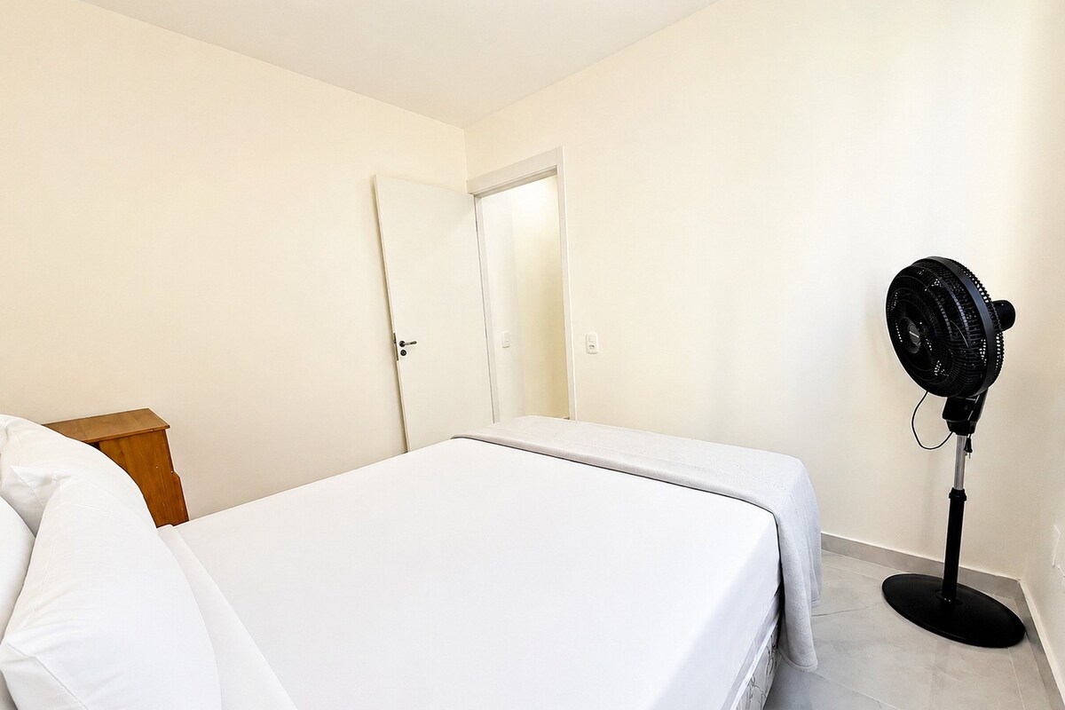 Una camera da letto con un letto, un comodino, una porta e una ventola da terra.