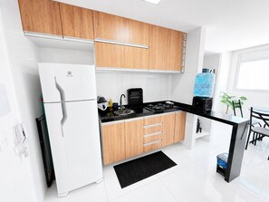 Une cuisine moderne avec des appareils électroménagers blancs, des meubles en bois, un plan de travail noir et un petit coin repas comprenant une table et des chaises.