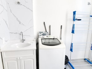 A bathroom with a sink, a washing machine, and a drying rack.