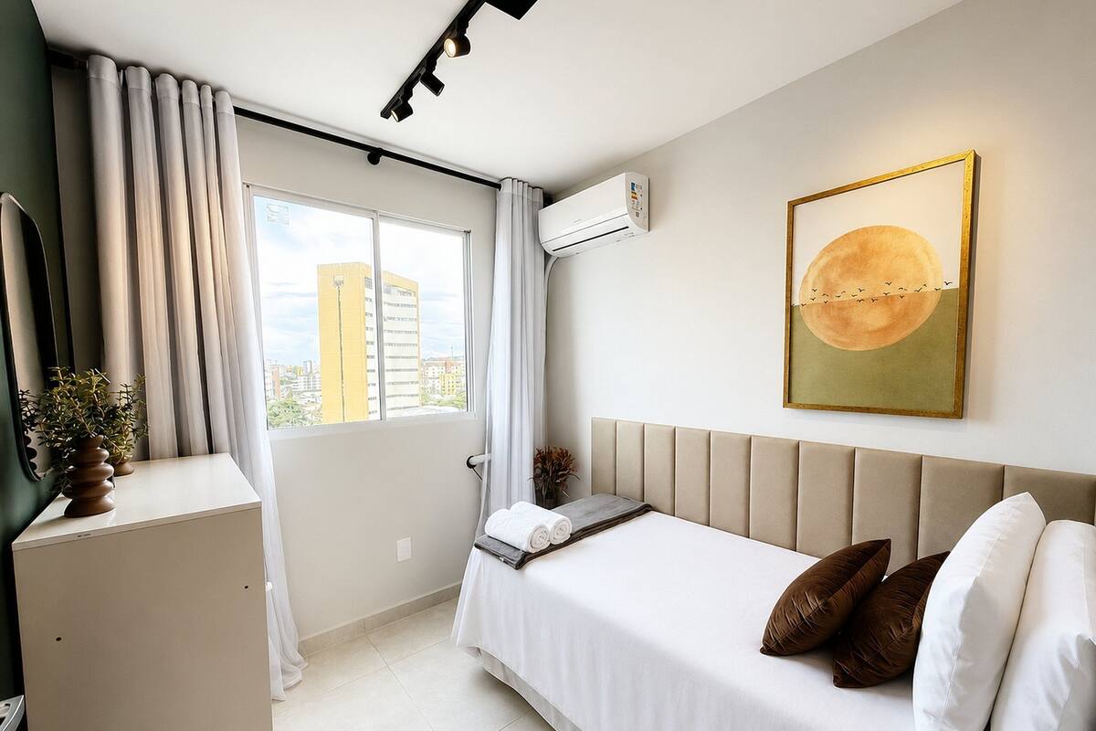 Una habitación de hotel moderna con cama, escritorio, ventana con cortinas, aire acondicionado y vista a la ciudad.