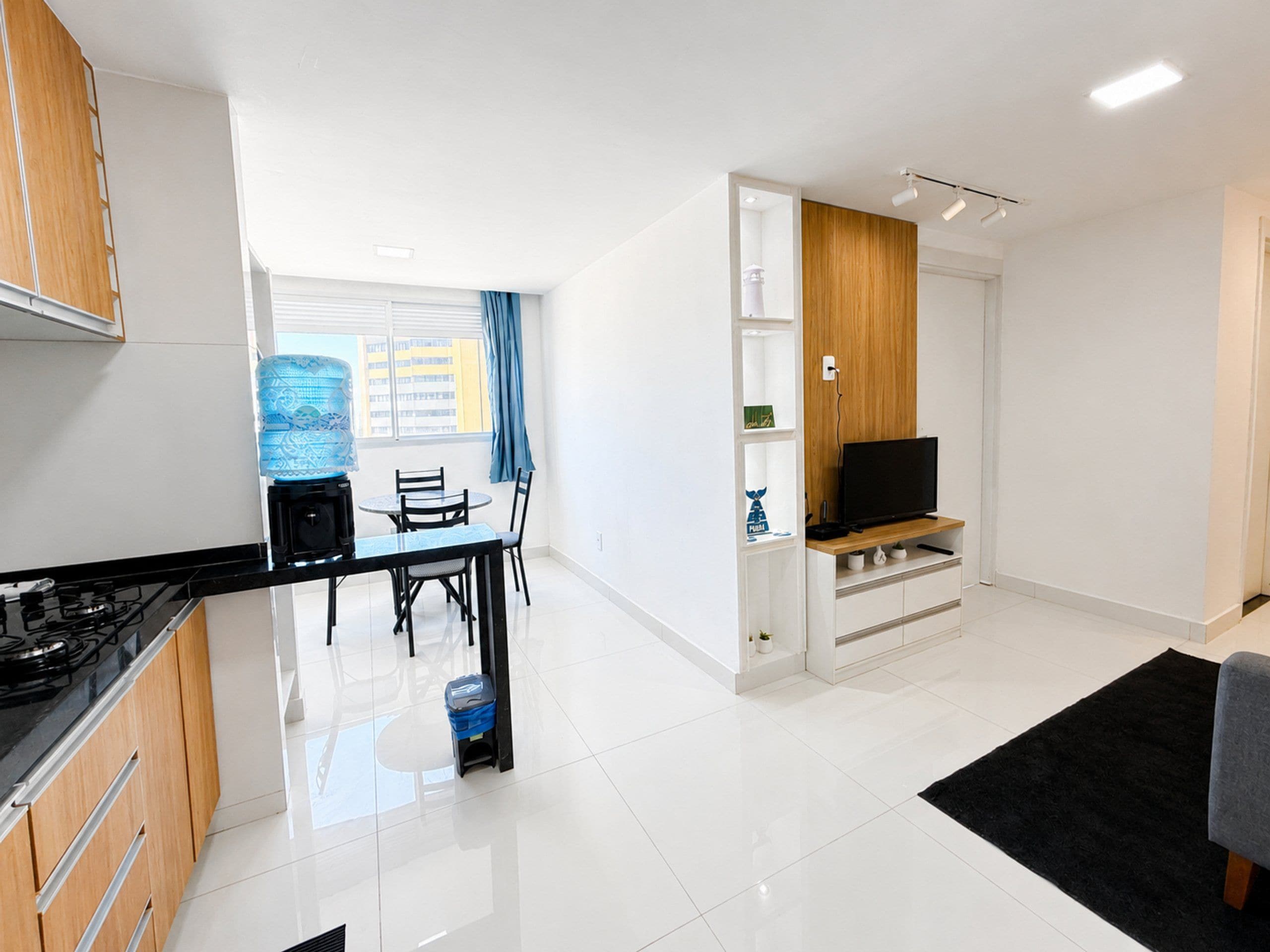 A modern kitchen with a dining area, a flat-screen TV, and a water dispenser.