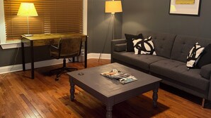 Una sala de estar con un sofá gris oscuro, una mesa de centro de madera, un escritorio con una lámpara y un ventilador de techo.