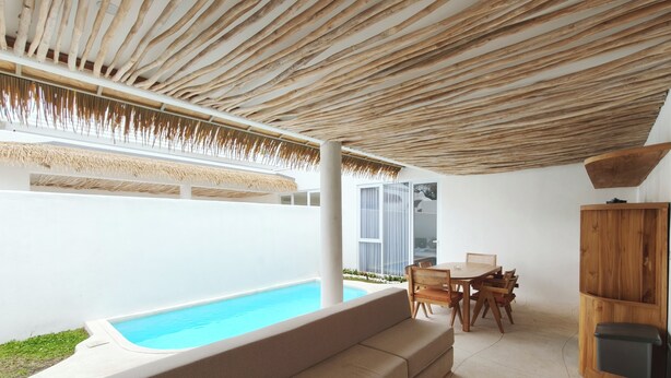 Un área de piscina moderna al aire libre con techo de madera, un banco integrado y una mesa de comedor con sillas.