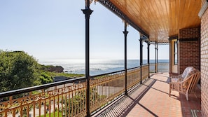 A balcony with a view of the ocean, featuring a wooden pergola, a brick wall, and a wicker chair.