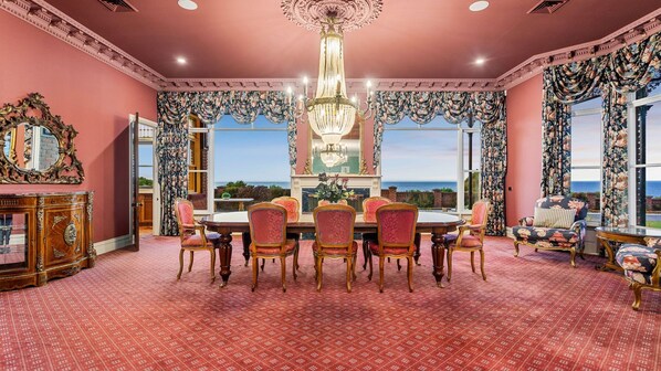 A dining room with a large table and chairs, a chandelier, and a view of the ocean.