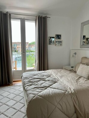 A hotel room with a bed, a nightstand, a mirror, and a window with curtains. - Beautiful house for 4 people with WiFi  et  11.50 m mooring (PORT GRIMAUD)
