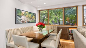 A dining area with a wooden table, cushioned benches, and a large window with a view of trees. - Newly Listed! Designer Mountain Retreat Steps from the Gondola. Great Winter Availability! (Aspen)