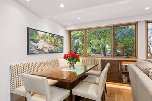 A dining area with a wooden table, cushioned benches, and a large window with a view of trees. - Newly Listed! Designer Mountain Retreat Steps from the Gondola. Great Winter Availability! (Aspen)