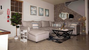 A modern living room with a sectional sofa, a coffee table, a plant, and artwork on the wall. - Spacious 4-bedroom townhome in tranquil Lakewood with AC (Lakewood)