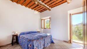 Een slaapkamer met een bed, een tafeltje, een lamp, een raam en een balkon.