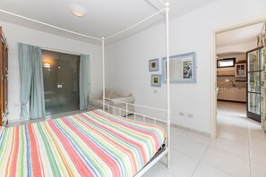 A bedroom with a four-poster bed, a glass shower enclosure, and a view into the kitchen. - Sale Marino - Goelba (Capoliveri)