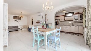Een ruime woonkamer met een eettafel, lichtblauwe stoelen en een kroonluchter.