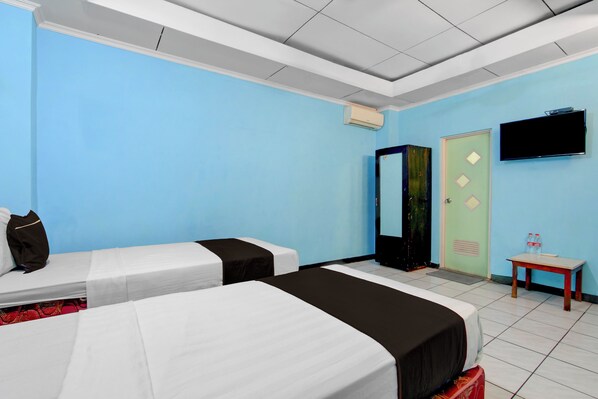 A hotel room with two beds, a television, a wardrobe, and a small table with bottles. - OYO 95140 Metro Guest House (Yogyakarta)