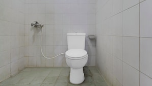 A small, white-tiled bathroom with a toilet, a wall-mounted faucet, and a toilet paper holder. - OYO 95140 Metro Guest House (Yogyakarta)