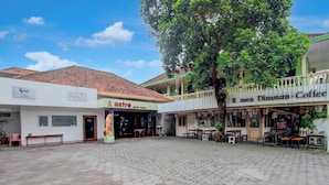 A courtyard with hexagonal paving, a tree, and buildings with signs for 'NALA' and 'R men Dimsum Coffee'. - OYO 95140 Metro Guest House (Yogyakarta)