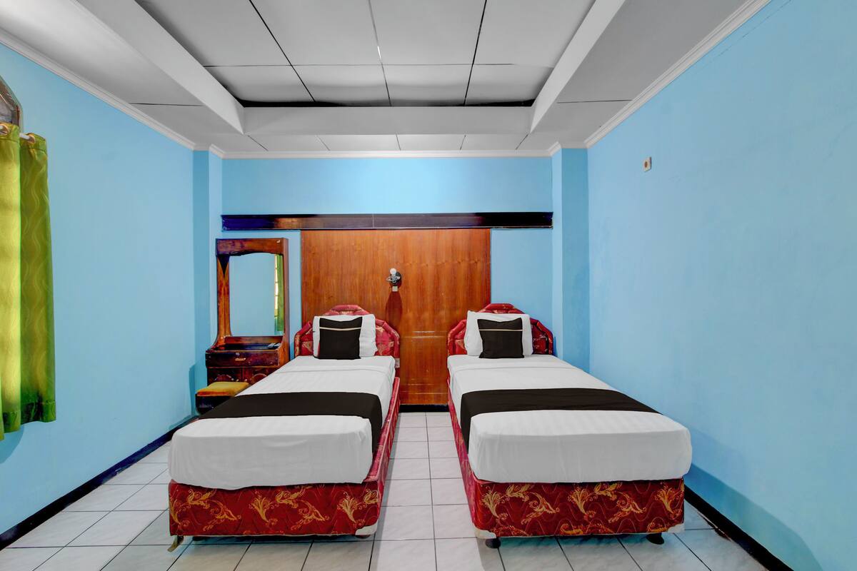 A room with two beds, a wooden door, and a mirror on the wall.