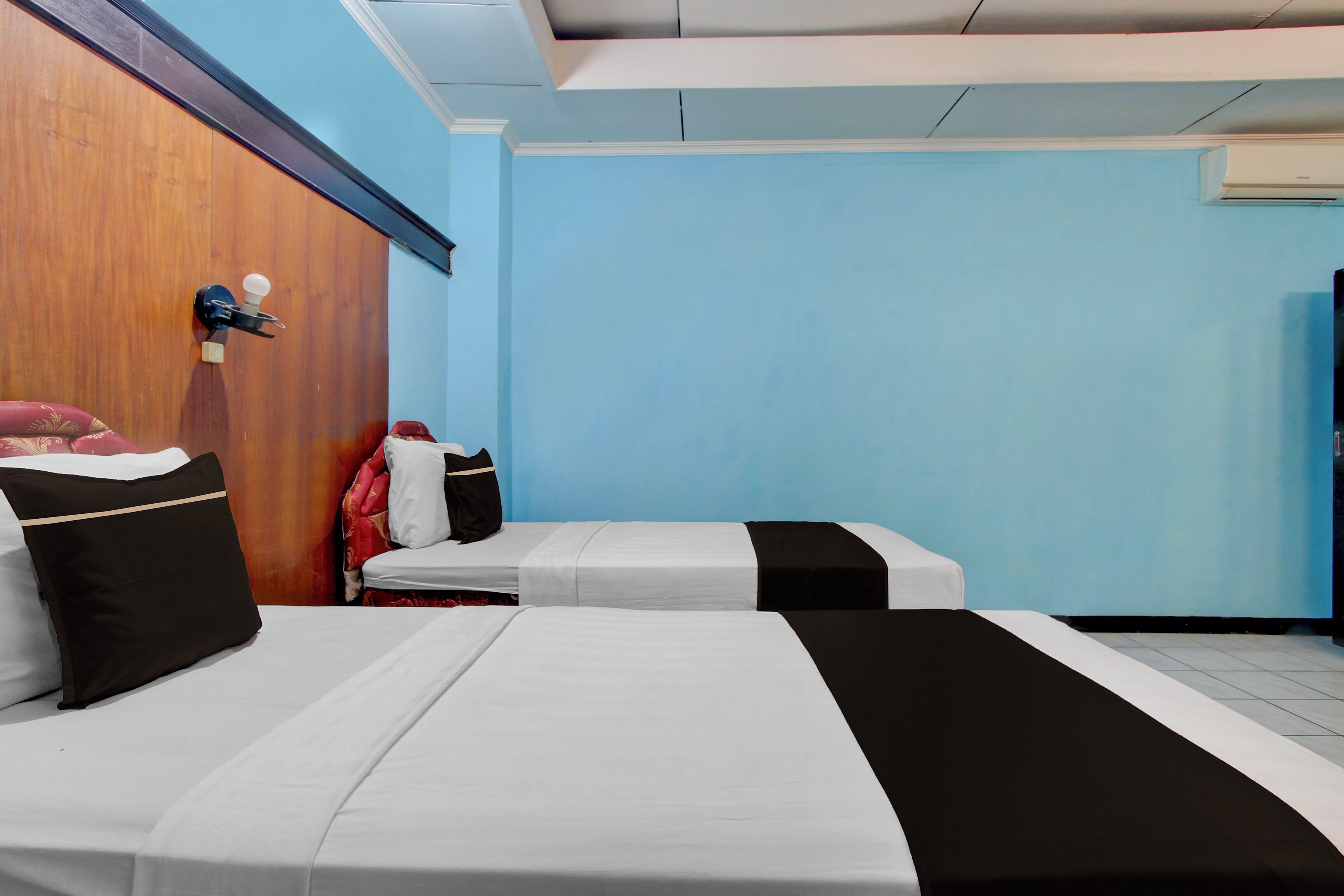 Habitación de hotel con dos camas, cabecero de madera, aire acondicionado instalado en la pared y una maleta roja.