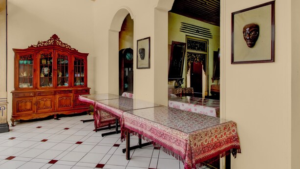 A room with a glass-top table, a wooden cabinet, and framed artwork on the walls. - OYO 95140 Metro Guest House (Yogyakarta)