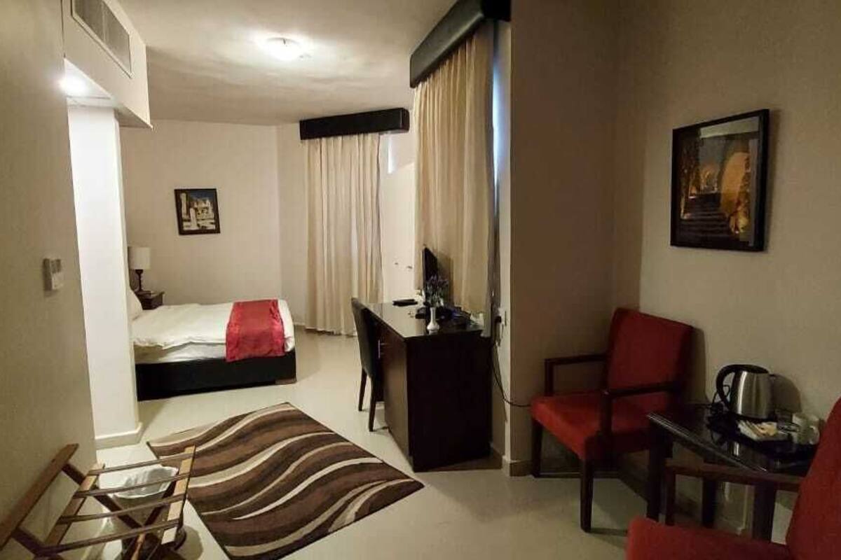A hotel room with a bed, desk, chair, and a small table with a kettle.