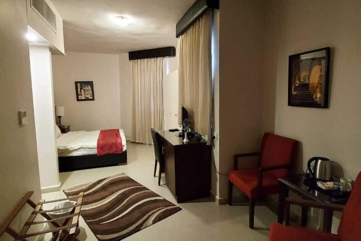 A hotel room with a bed, desk, chair, and a small table with a kettle.