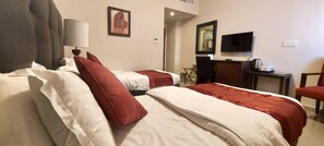 A hotel room with two beds, a desk, a television, and a chair. - La Maison Hotel (Wadi Musa)