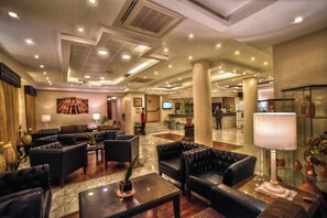 A hotel lobby with leather sofas, a reception desk, and a TV screen. - La Maison Hotel (Wadi Musa)