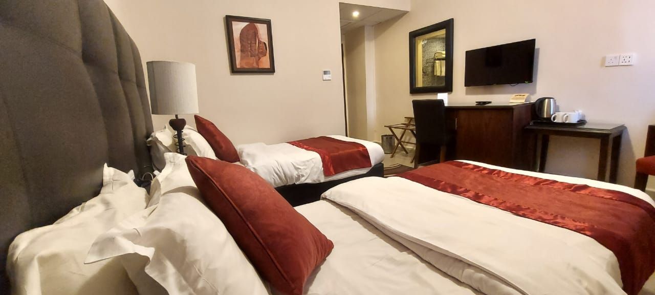 A hotel room with two beds, a desk, a chair, a TV, and a lamp.