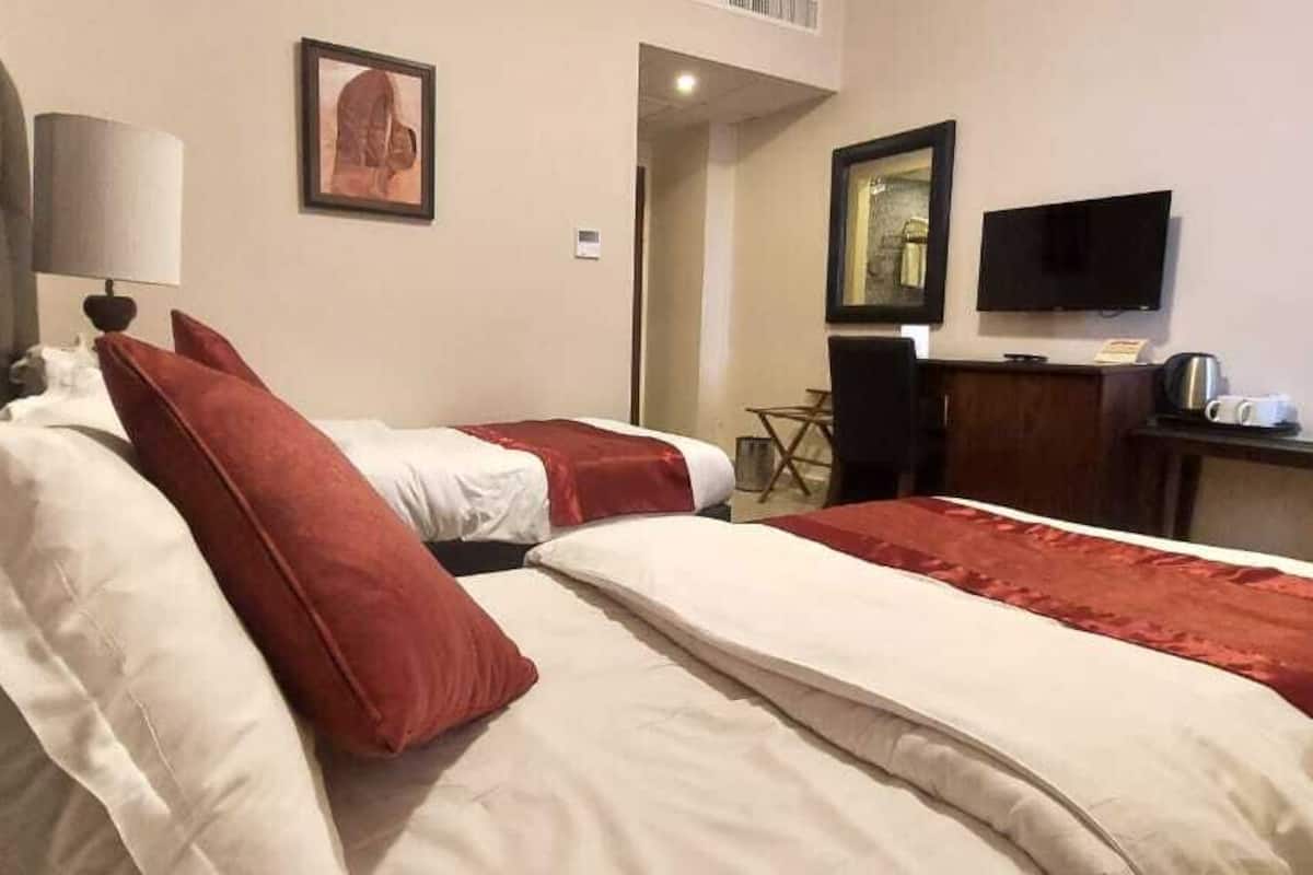 A hotel room with two beds, a desk, a television, and a chair.