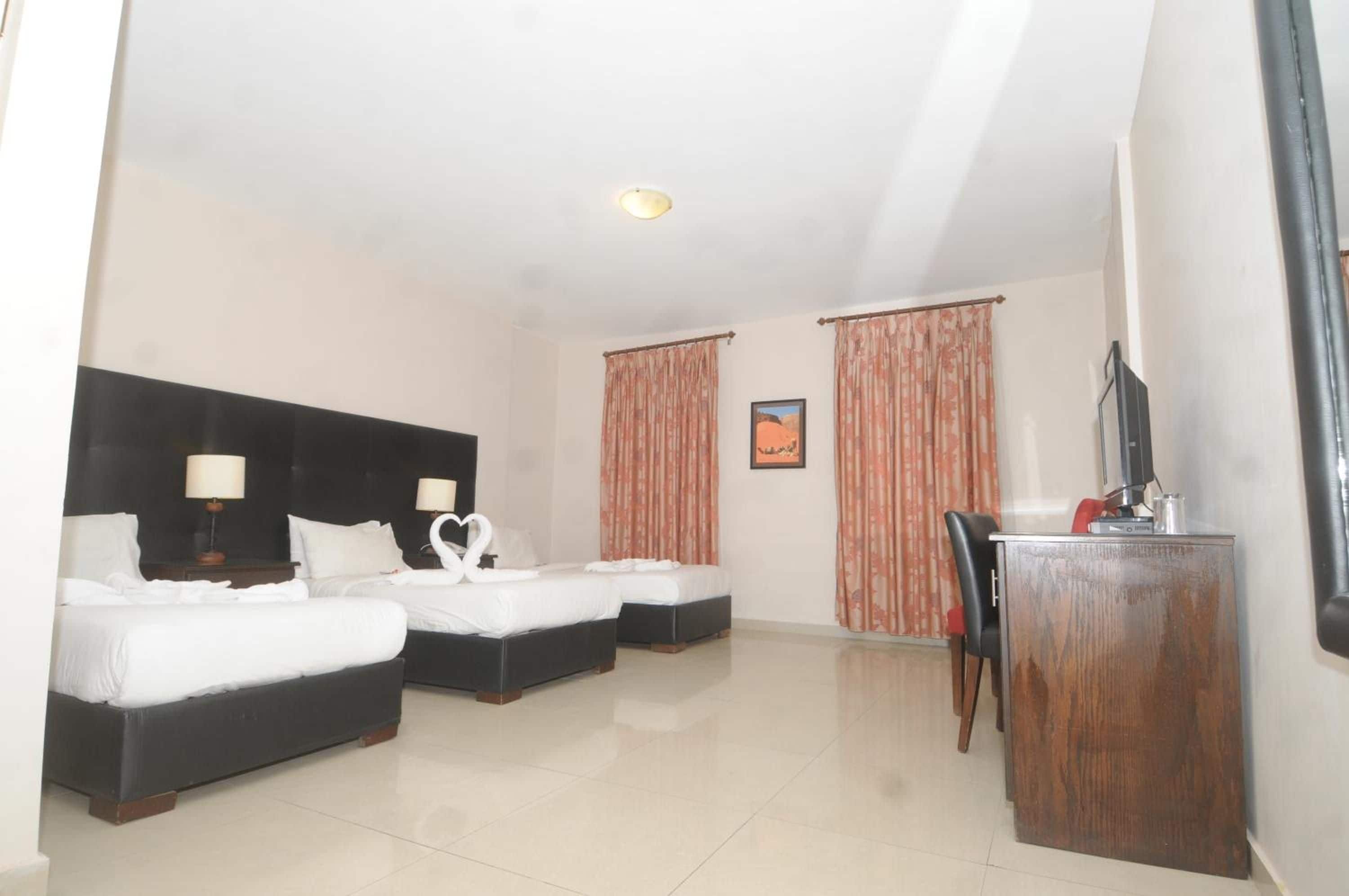 A hotel room with two beds, a desk, a chair, a television, and curtains.