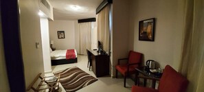 A hotel room with a bed, desk, chair, and a small table with a kettle. - La Maison Hotel (Wadi Musa)