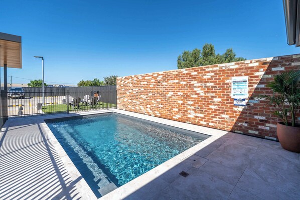 A rectangular swimming pool with clear blue water, surrounded by a brick wall and a metal fence.