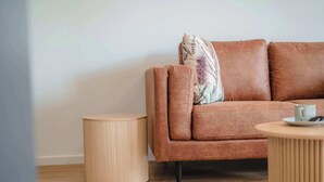 Una sala de estar moderna con un sofá de cuero marrón, una mesita redonda de madera y un taburete a juego.