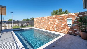En rektangulär swimmingpool med klart, blått vatten, omgiven av en mur av tegelsten och ett staket av metall.