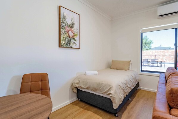 Un dormitorio con cama, una silla, un sofá, un ventanal con vistas y un cuadro en la pared.
