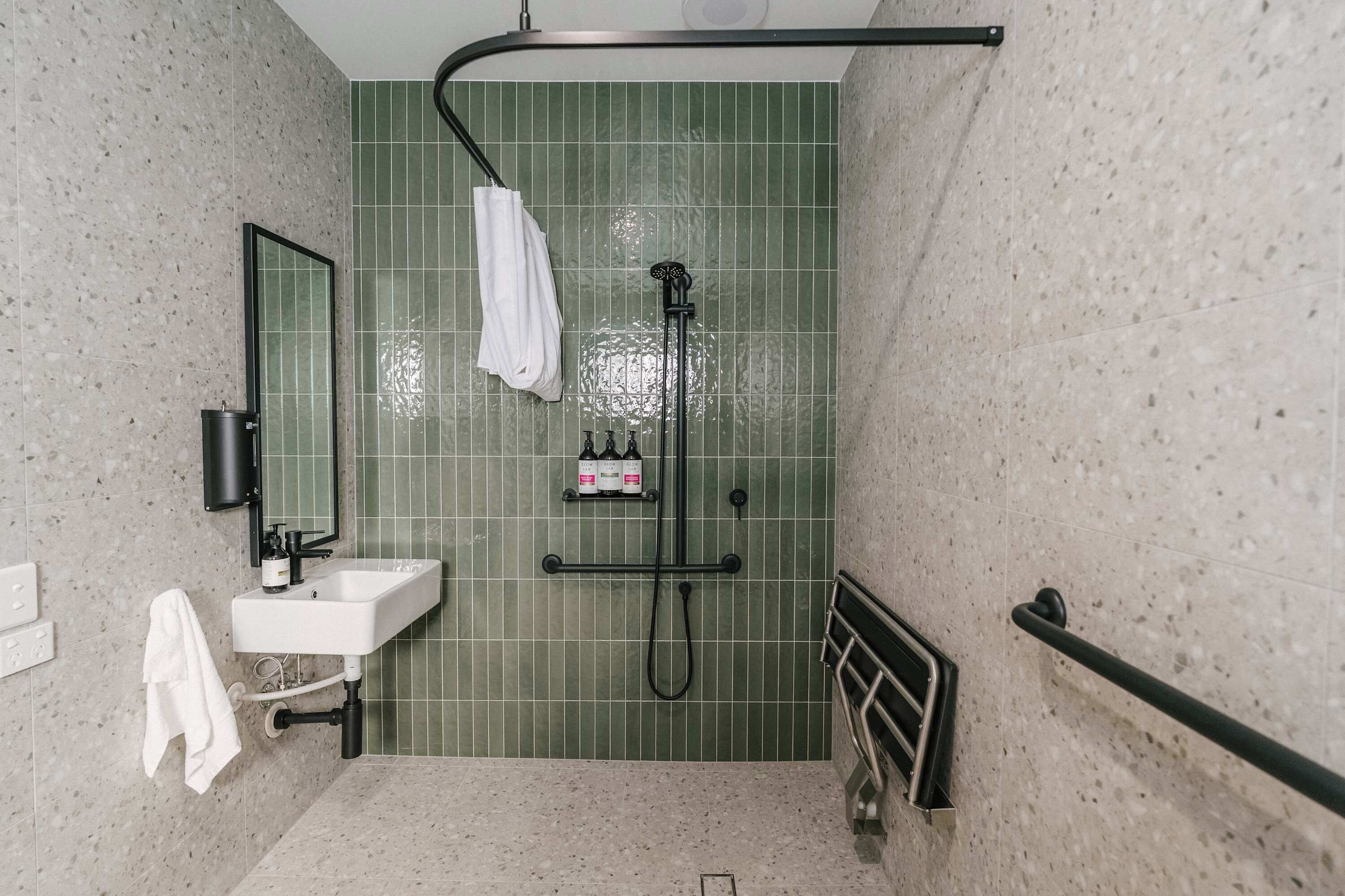 Un baño con un lavabo blanco, un espejo, un perchero para toallas y una ducha con cabezal de ducha manual.
