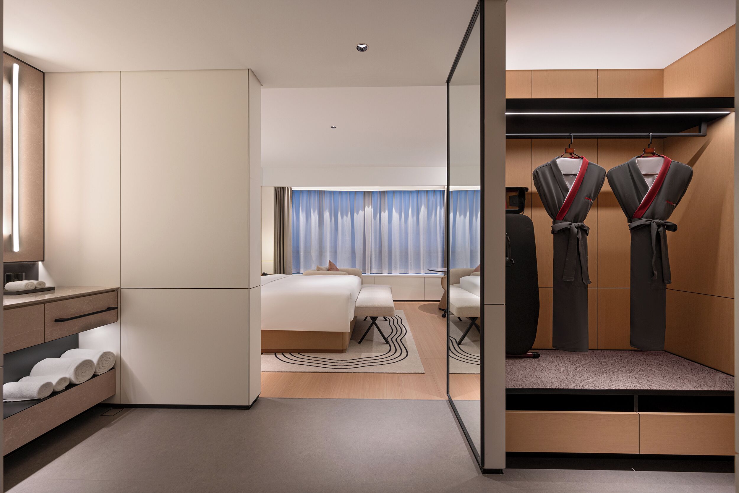 A modern hotel room with a bed, seating area, and a walk-in closet with hanging garments.