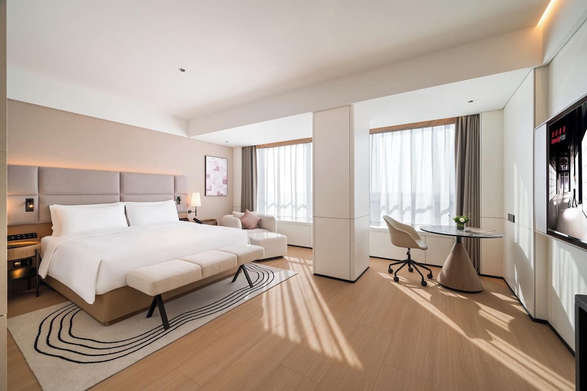 A modern hotel room with a large bed, a sofa, a desk, and a TV.