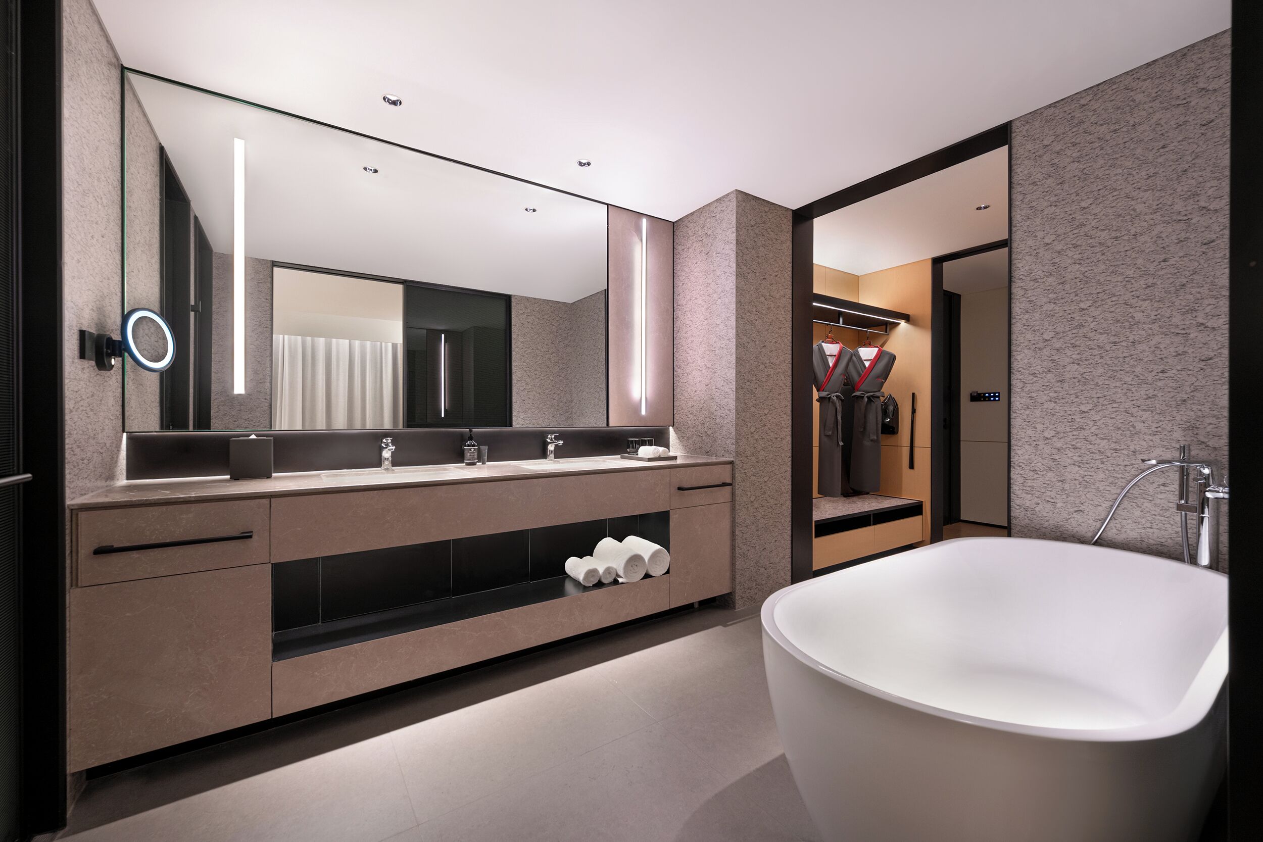 A modern bathroom with a freestanding bathtub, a large mirror, and a vanity with a built-in shelf.
