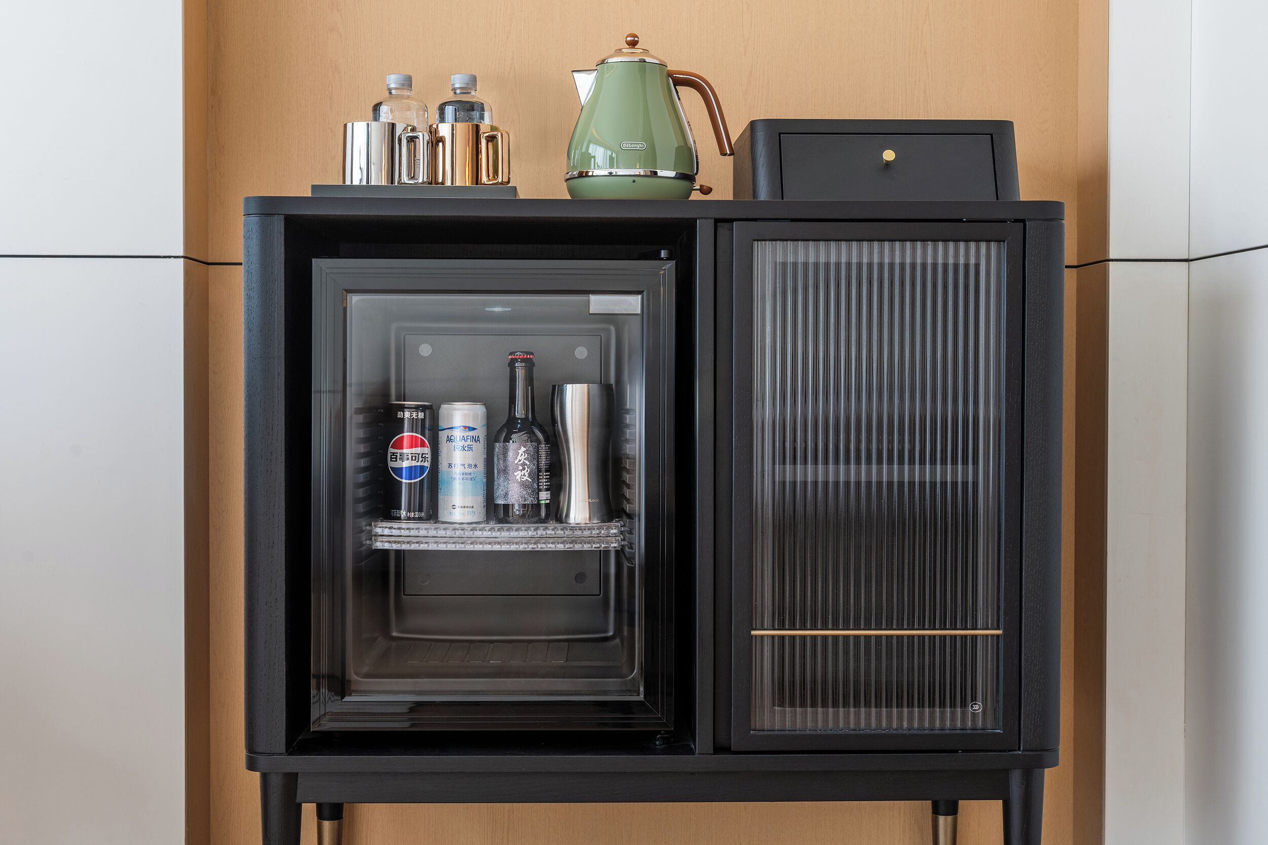 Een minibar met een koelkast, koffiezetapparaat en diverse flessen.