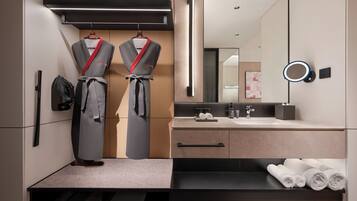 A modern bathroom with a large mirror, a towel rack with robes, a sink with a countertop, and a towel shelf.